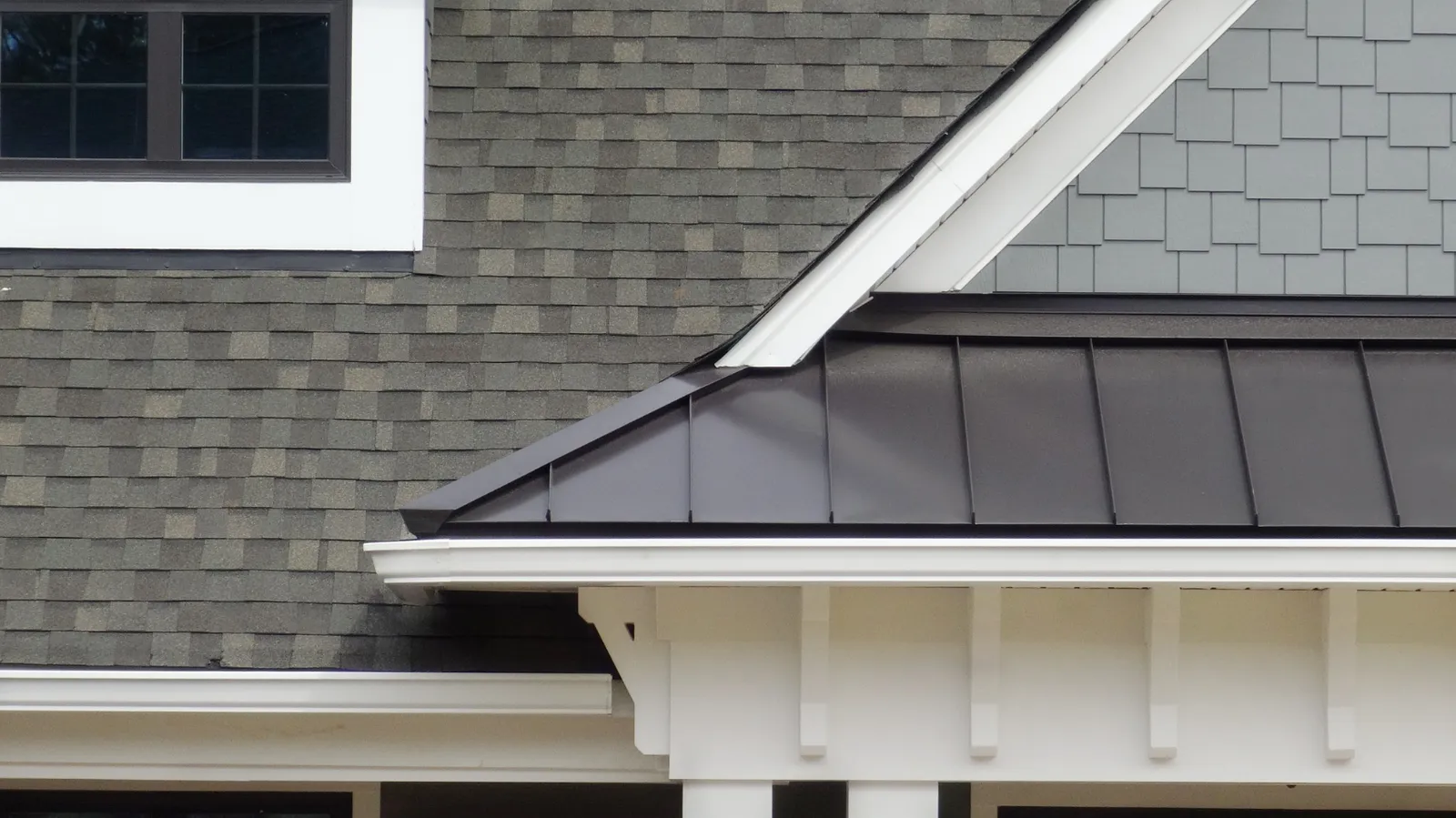 A gray shingle roof joining a dark standing seam roof with white trim