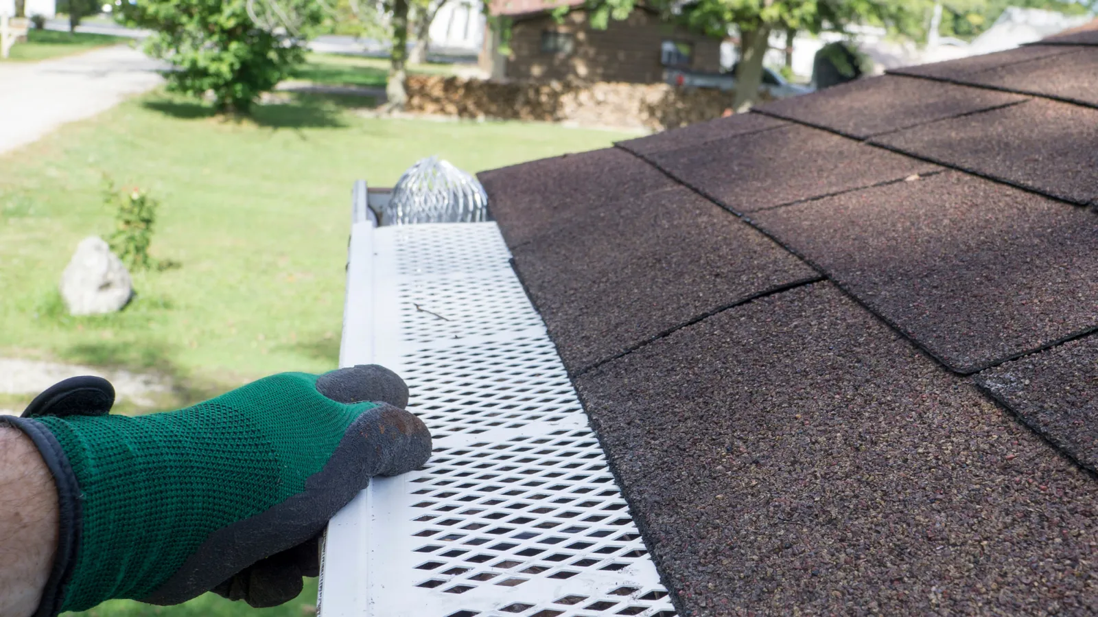 Gloved hand of a roofer fastening perforated gutter guard